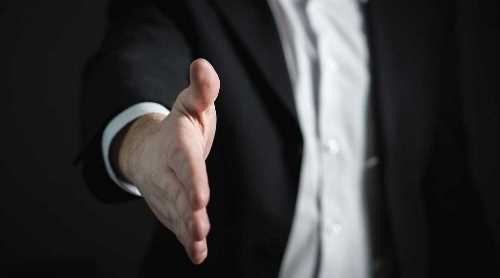 Person in a suit reaching out to shake hands.