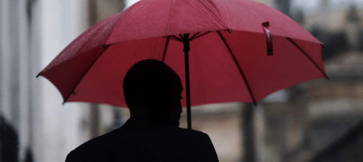 Dark sillhouette of a man holding a red umbrella.