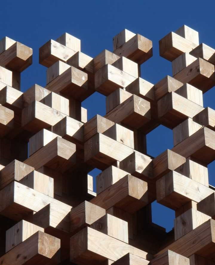 wooden building blocks stacked in a geometrical pattern against a clear blue sky