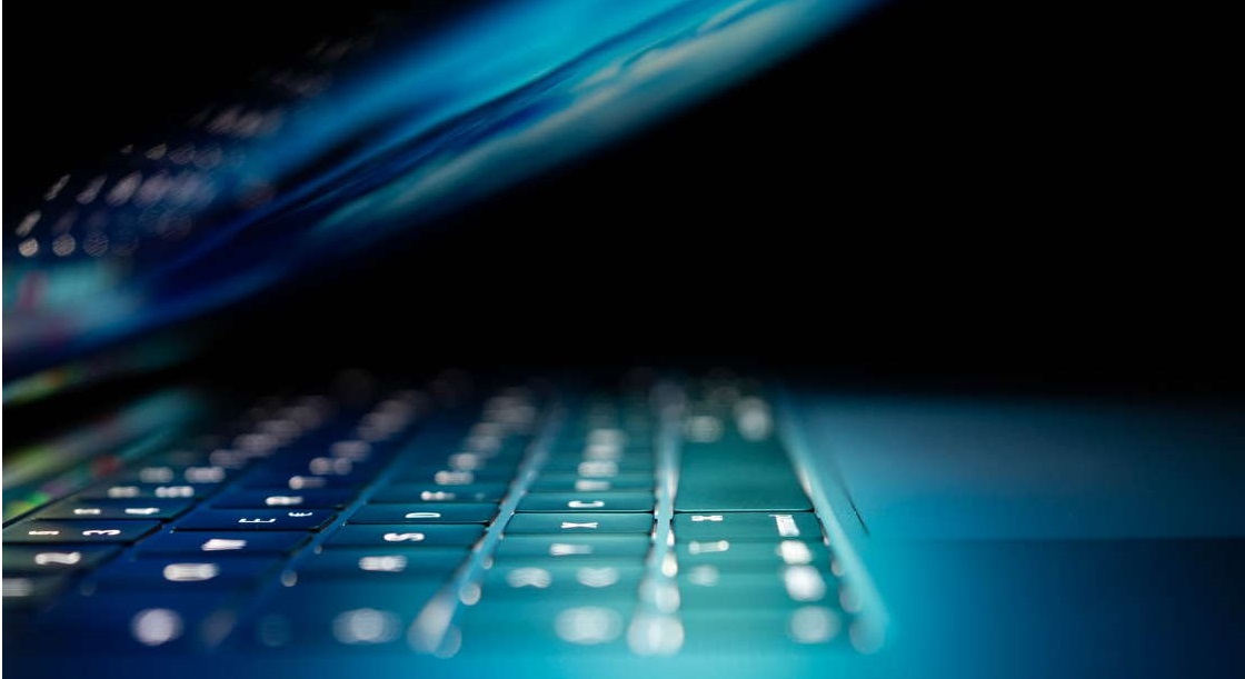 Lit up laptop with blue light in a dark room.