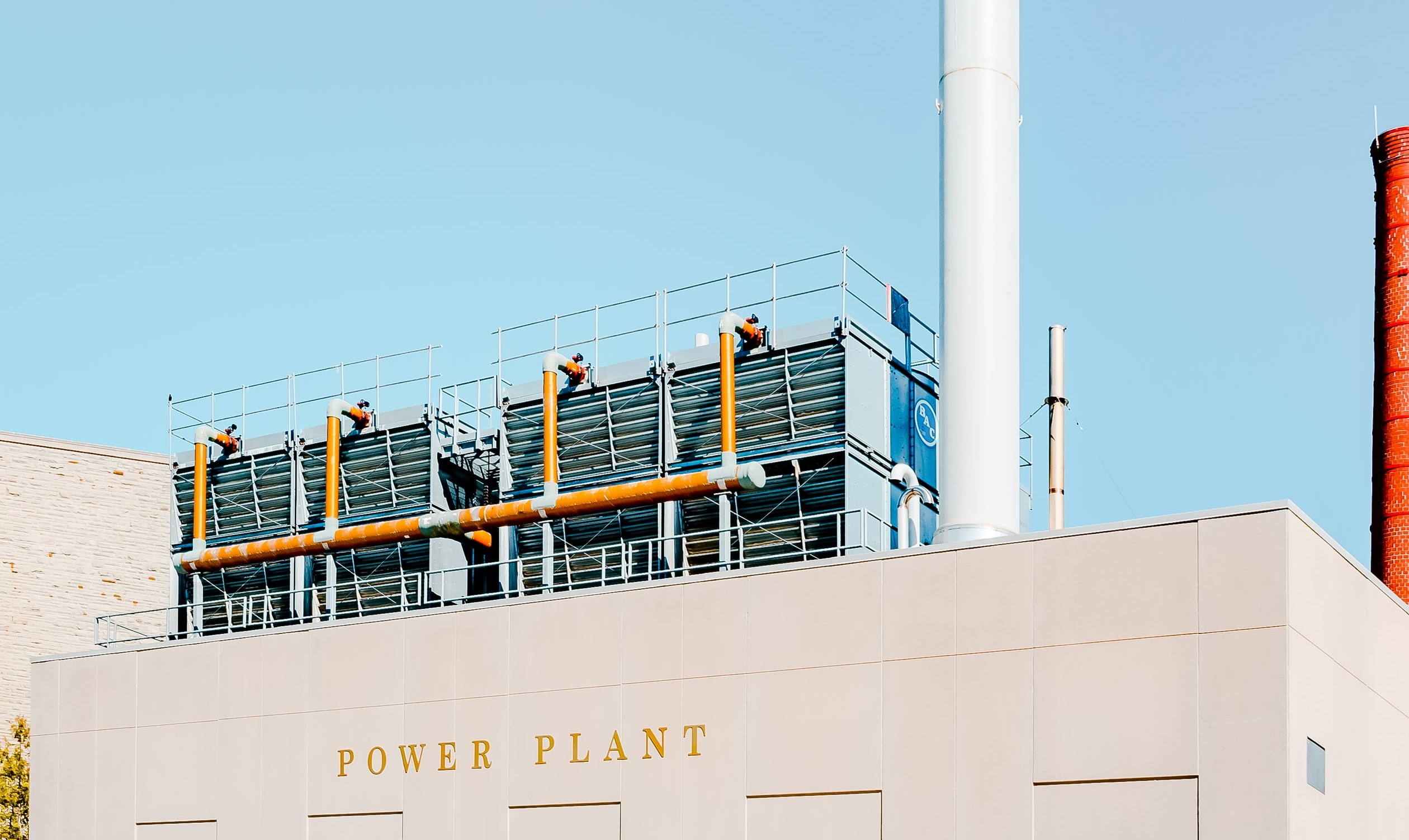 Tidy power plant building with orange pipes against a clear blue sky.