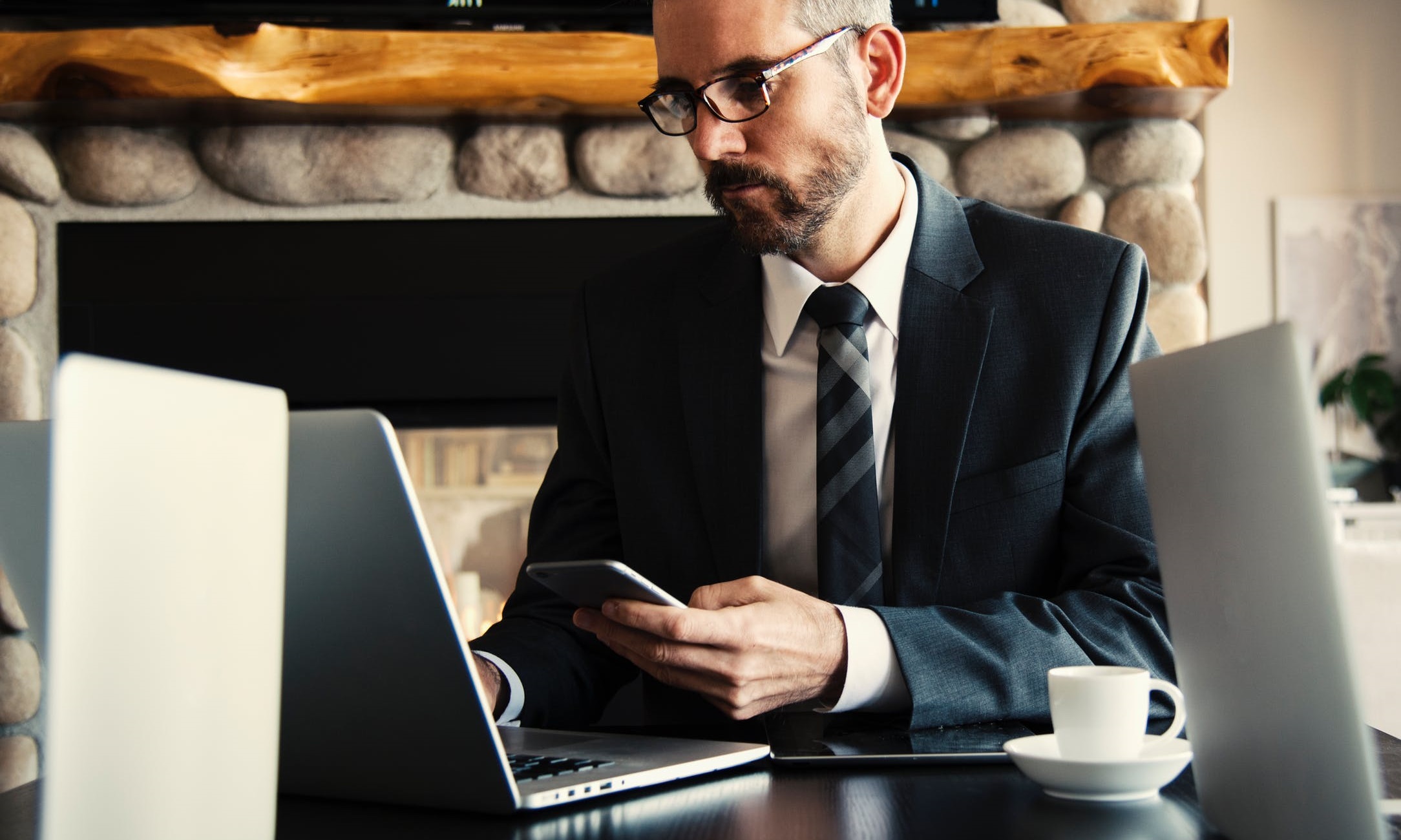 Businessman working on phone and laptop at a wooden table.