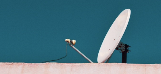 White satellite dish against a very blue sky, on top of a pink building