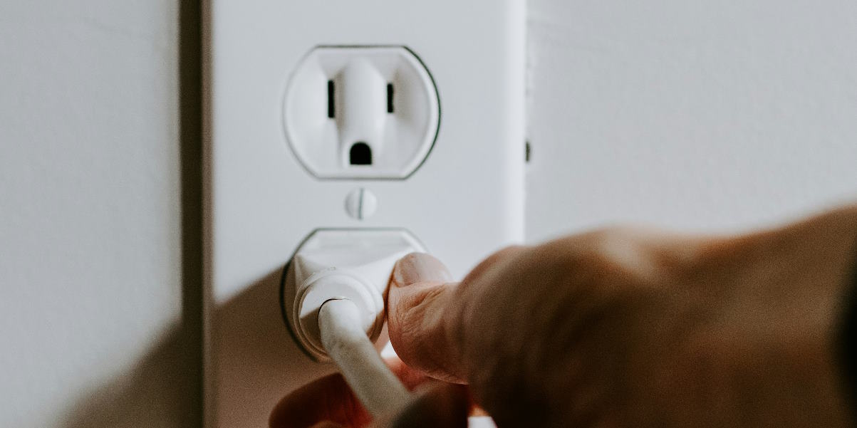A hand about to pull a plug out of wall socket.