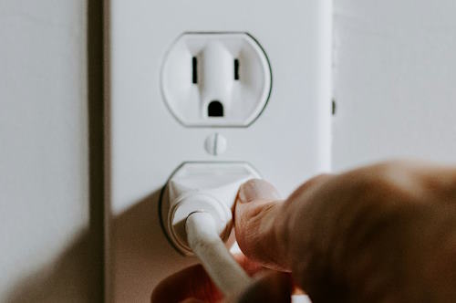 A hand pulling a plug from a wall socket