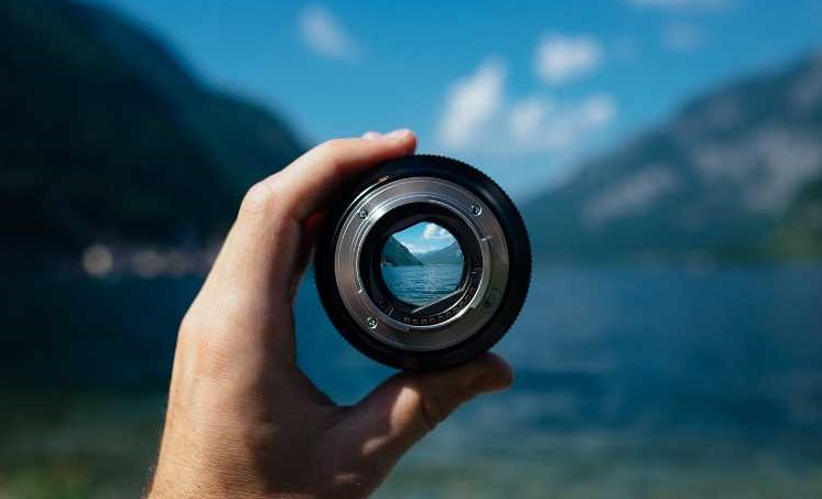 Man focusing on mountain range using a camera lens