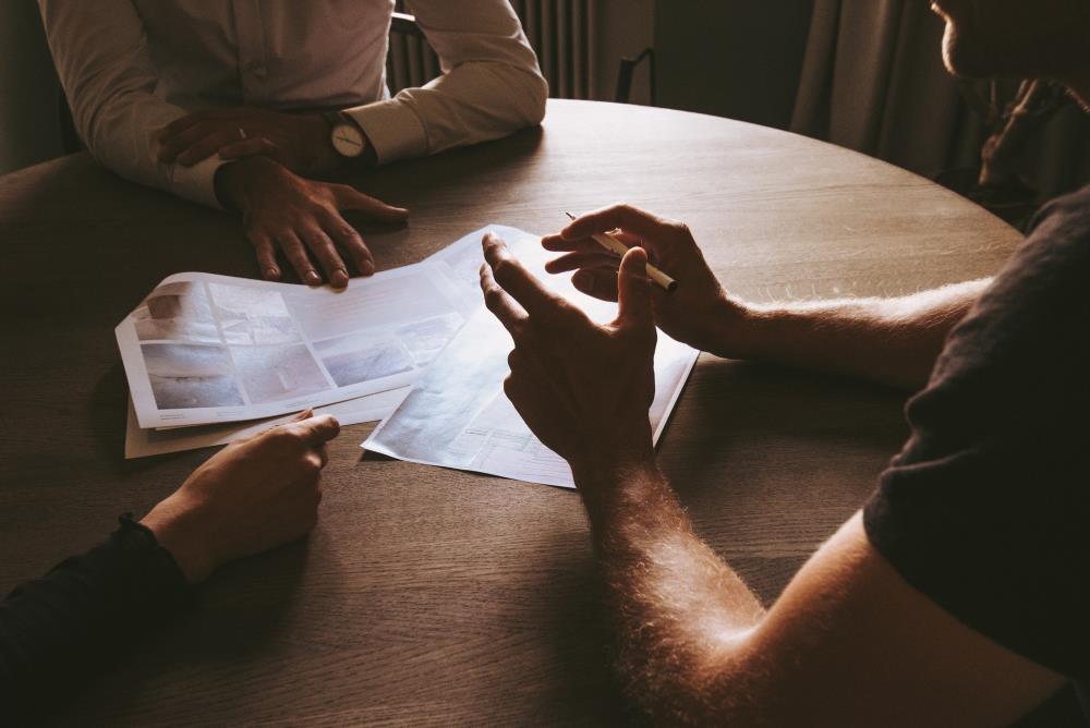 Closeup of a round table with three people sitting around some paperwork