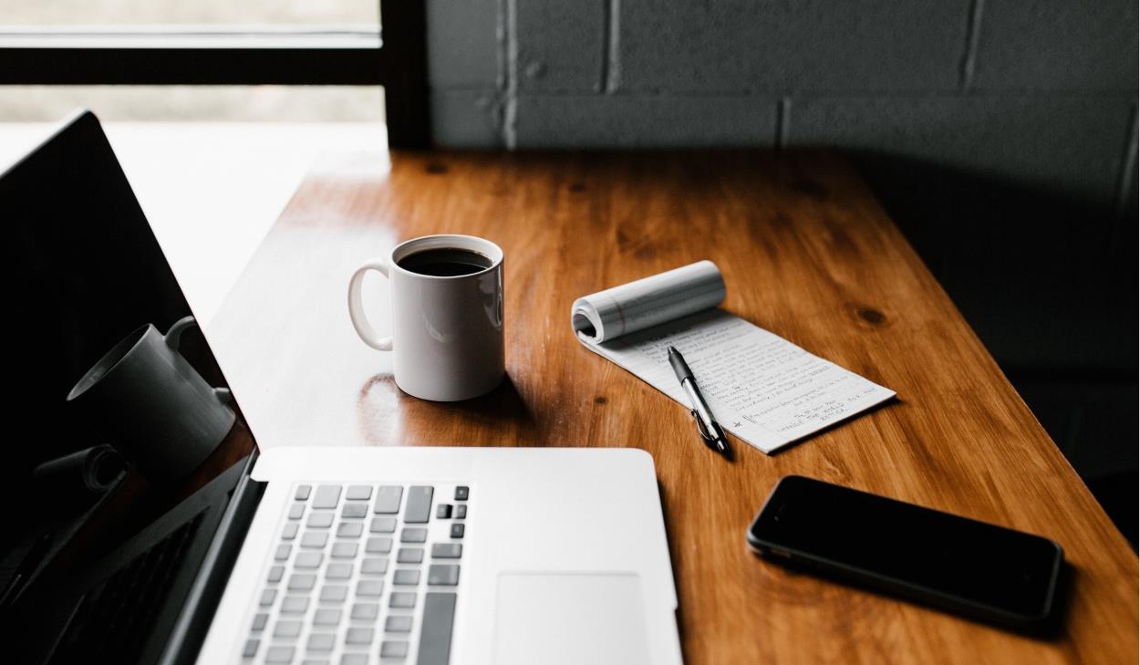 Laptop, coffee, and a notepad on a wooden table.