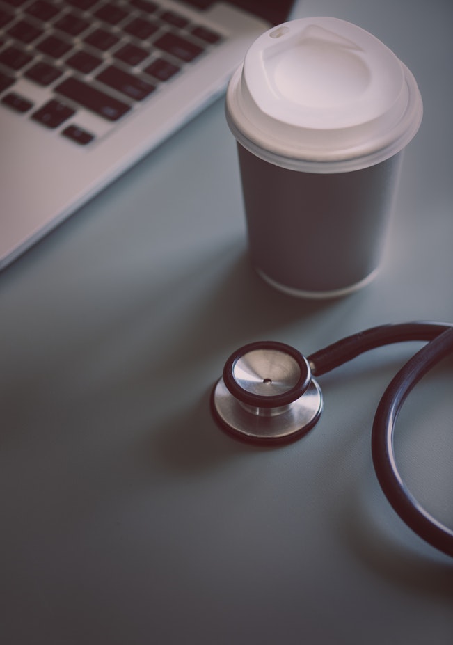 Stethoscope, coffe cup, and laptop on top of a desk