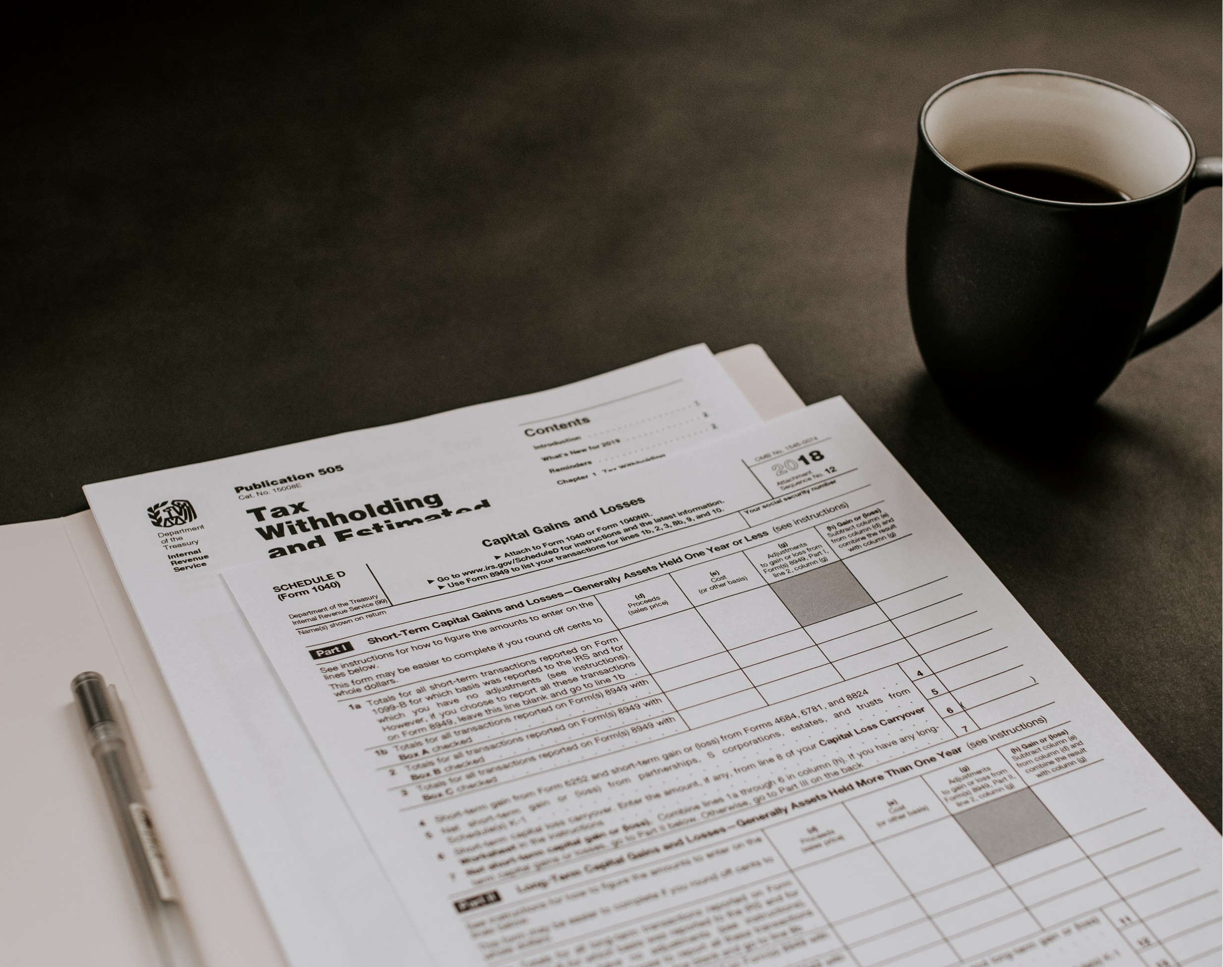 Photo of a documents and forms, a pen, and a cup with coffee on a dark surface.