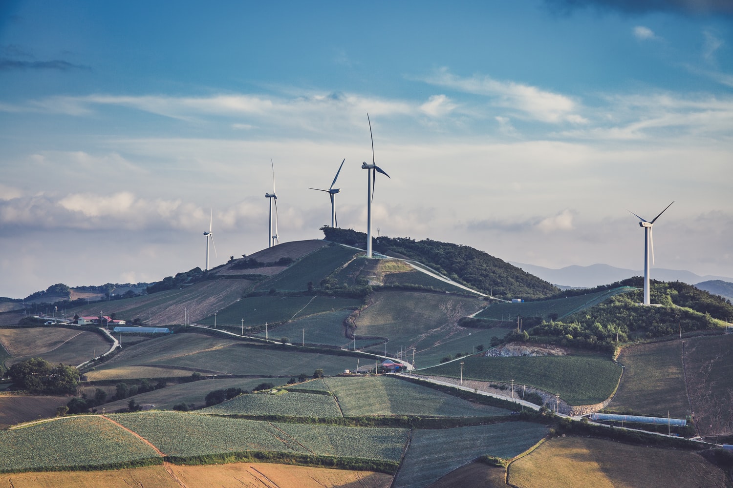 A photo of wind turbines on a green hilly lanscape, against a blue sky.