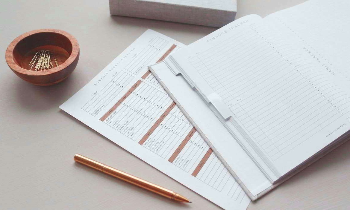 Closeup photo of neat documents, a wooden bowl of paperclips, and a a pen.