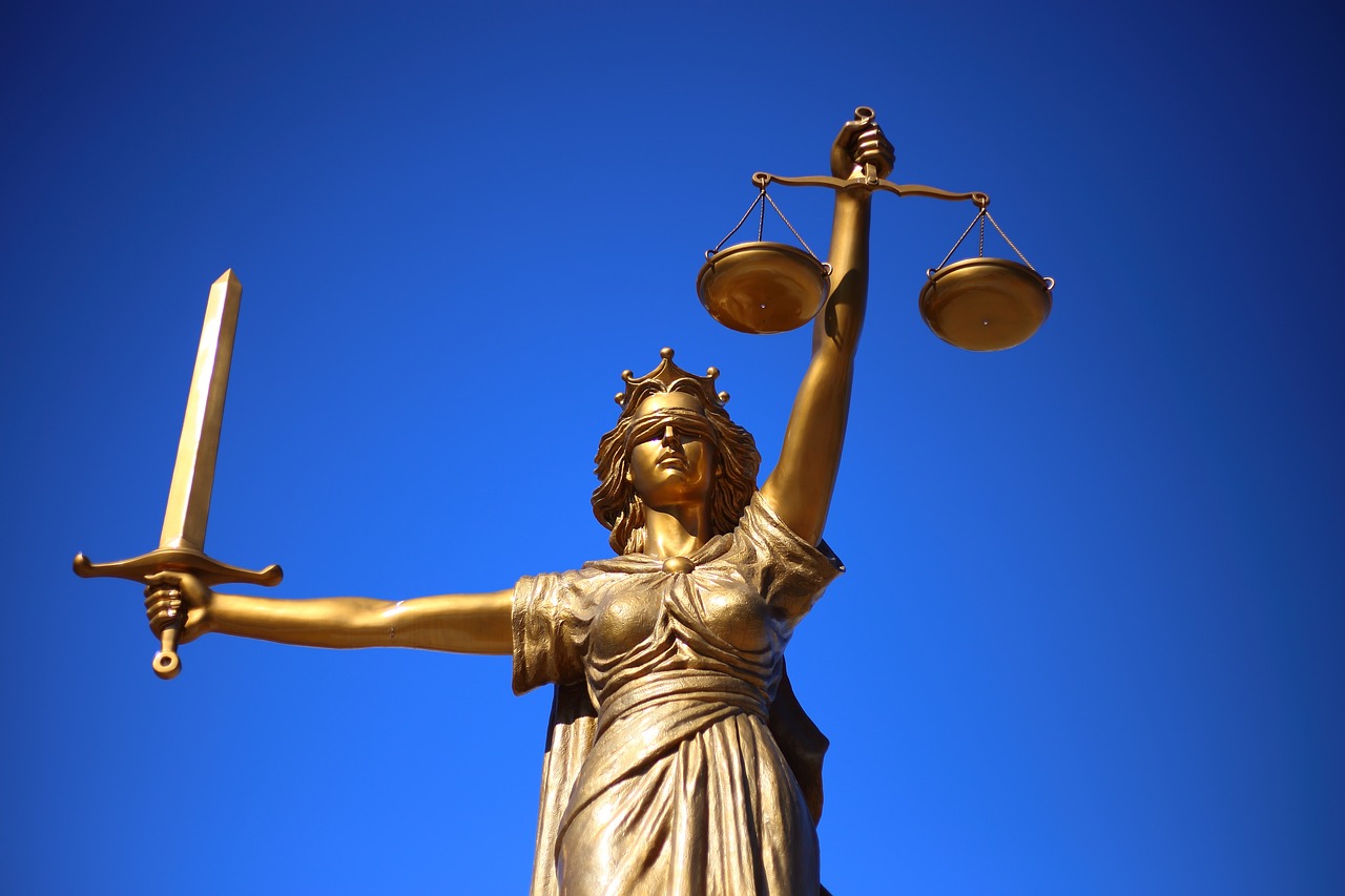 Photo of a gold statue representing justice as a biln woman, holding a sword and scales, against a very blue sky.